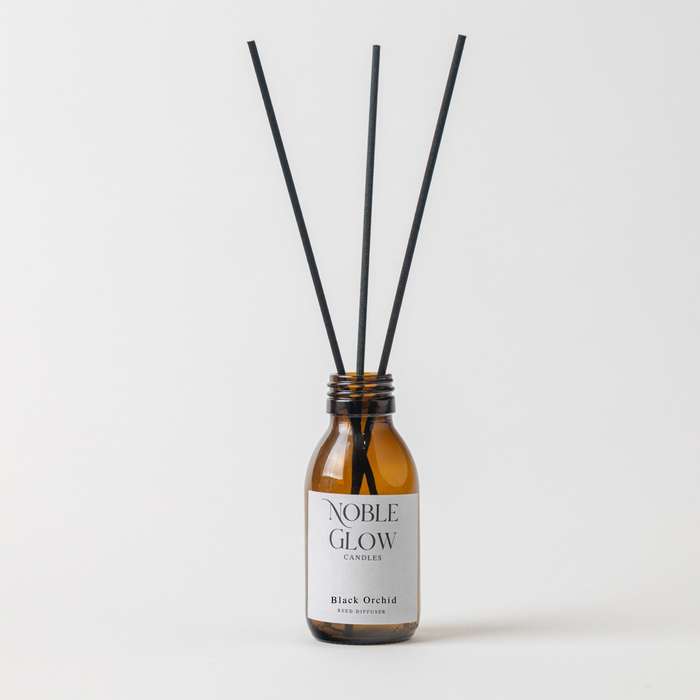Reed diffuser with black sticks in a brown bottle labeled 'Noble Glow Candles' on a white background