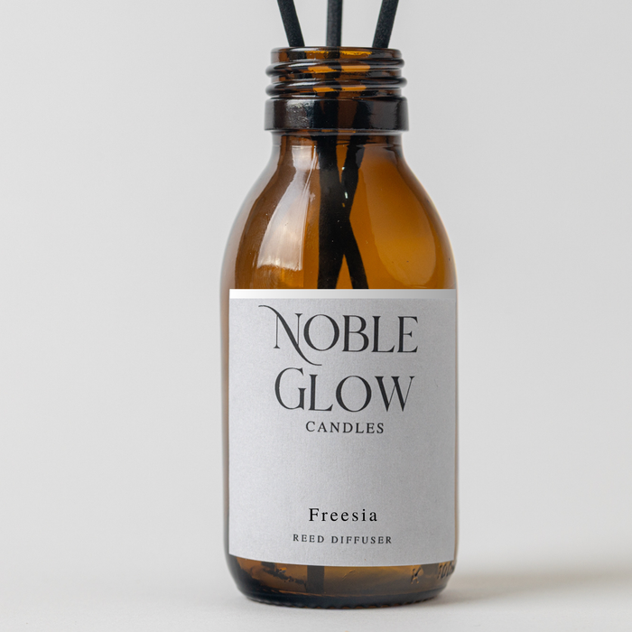 Reed diffuser bottle labeled 'Noble Glow Candles' with Freesia fragrance on a light gray background