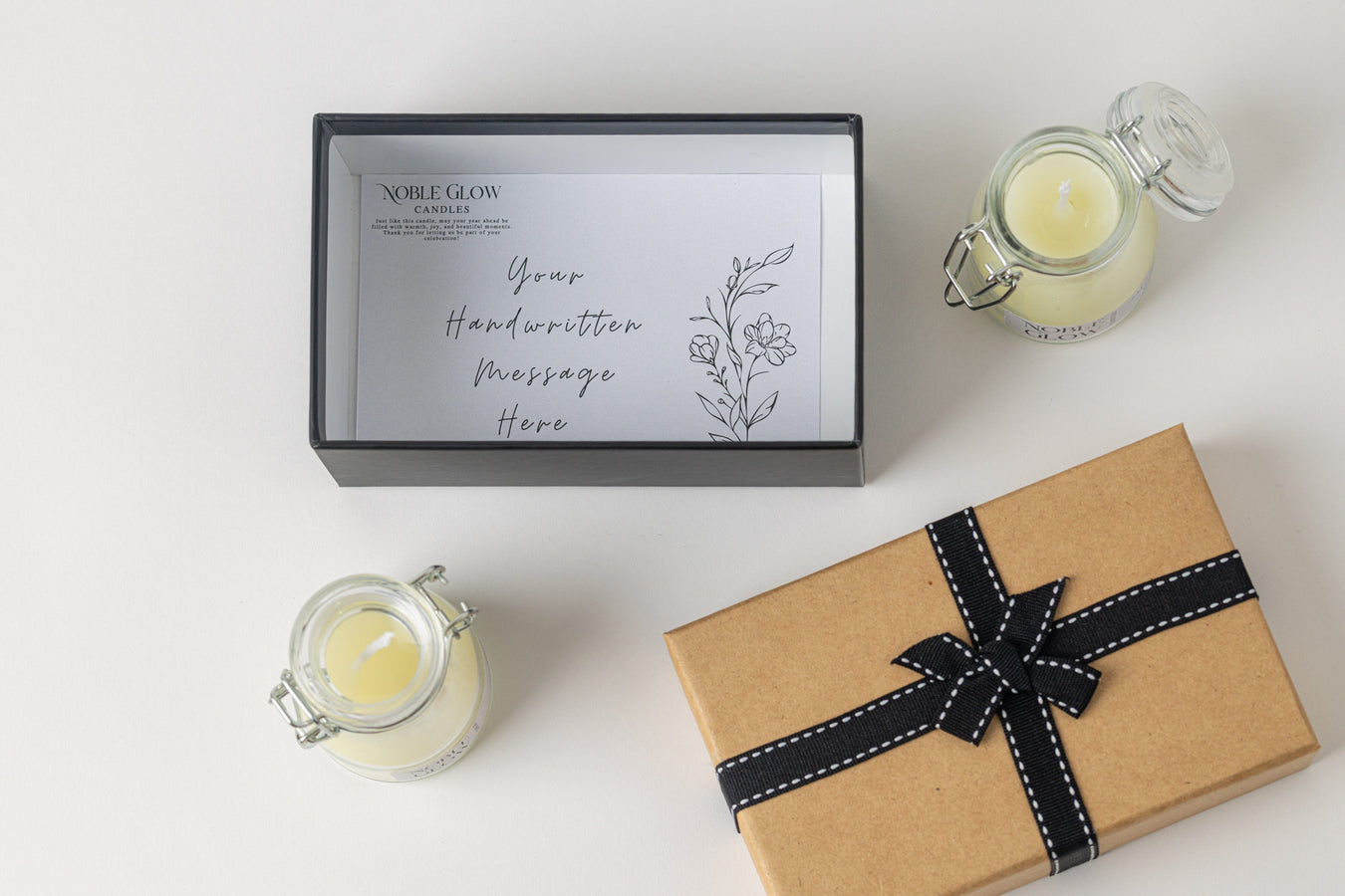 Gift box with a black ribbon, two candles, and a card on a white surface